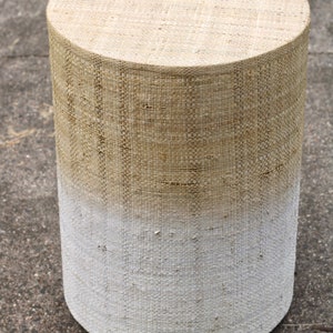 May include: A round, woven stool with a white ombre effect. The stool is made of natural fibers and has a rustic, farmhouse style.