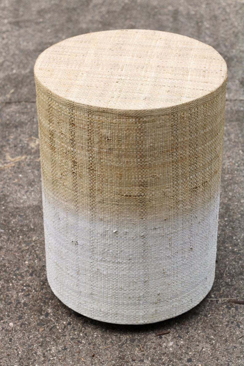 May include: A round, woven stool with a white ombre effect. The stool is made of natural fibers and has a rustic, farmhouse style.