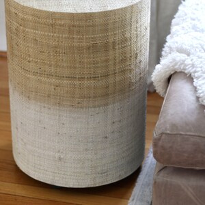 May include: A round, woven side table with a natural beige top and a white bottom. The table is made of natural materials and has a rustic, farmhouse style.