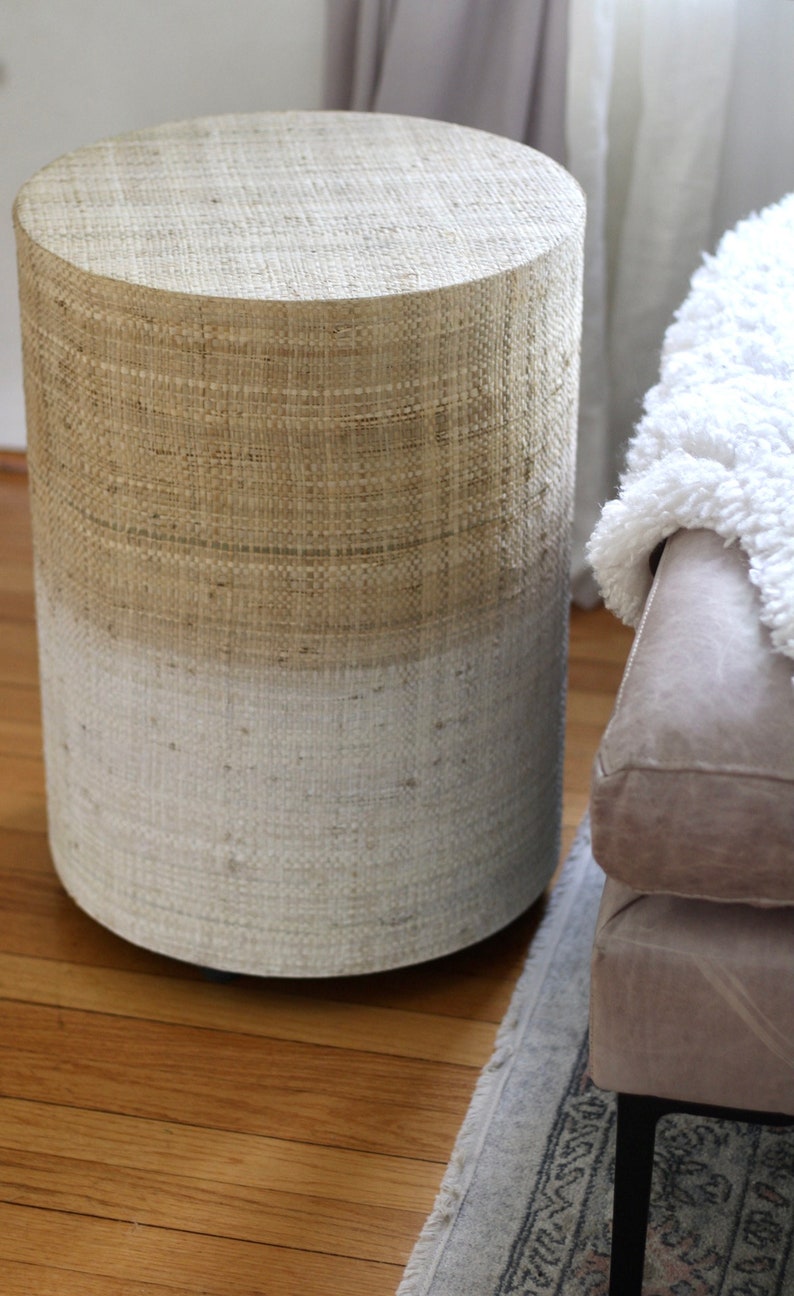 May include: A round, woven side table with a natural beige top and a white bottom. The table is made of natural materials and has a rustic, farmhouse style.