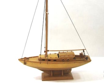 May include: A wooden model sailboat with a single mast and sails. The sailboat is on a wooden base and has a detailed hull.