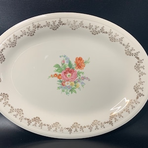 May include: White oval serving platter with a gold floral border and a colorful floral design in the center.
