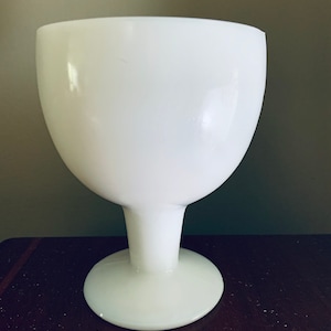 May include: A white opaque glass vase with a wide bowl and a short, thick stem. The vase has a round base.