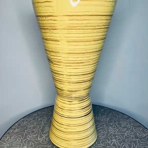 May include: A yellow ceramic vase with brown stripes. The vase has a wide mouth and a narrow base.