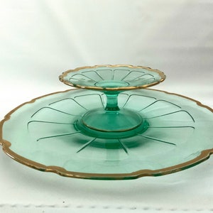 May include: Two-tiered serving tray made of clear green glass with a gold rim. The top tier is smaller and sits on a pedestal.