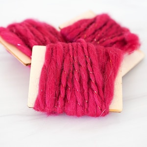 May include: Three spools of pink yarn with gold glitter thread wrapped around wooden spools.