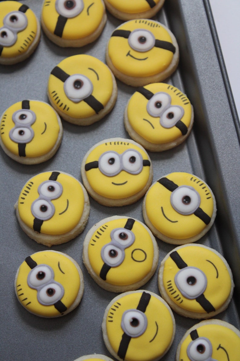 May include: A tray of yellow and black Minion-themed sugar cookies. The cookies are decorated with white eyes, black goggles, and a black mouth.
