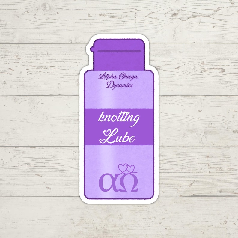 K&ouml;nnte beinhalten: Ein violetter Aufkleber mit dem Text "knotting Lube" in einer stilisierten Schriftart. Der Aufkleber enth&auml;lt auch den Text "Alpha Omega Dynamics" und ein Symbol aus zwei Herzen &uuml;ber den griechischen Buchstaben Alpha und Omega.