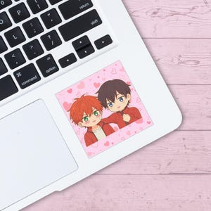May include: A sticker featuring two anime-style characters in red jackets and white shirts, set against a pink background with heart shapes. One character has orange hair and green eyes, the other has dark hair and blue eyes.