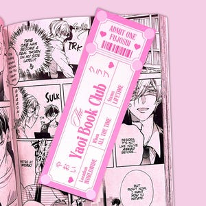 May include: Pink bookmark with the text "The Yaoi Book Club" and "Admit One Fujoshi." The bookmark is shaped like a ticket and features Japanese text and heart icons. The background is a manga page.
