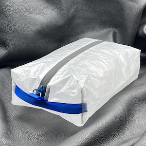 May include: A clear, translucent, rectangular pouch with a zipper closure and a blue webbing strap. The pouch is made of a lightweight, waterproof material.
