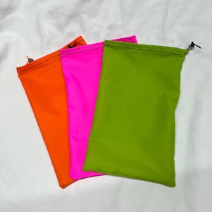 May include: Three brightly colored drawstring bags in orange, hot pink, and green. Each bag is rectangular with a drawstring closure at the top. The bags are made of a lightweight, possibly nylon, material.
