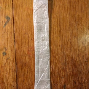 Puede incluir: Una bolsa rectangular transl&uacute;cida con cierre de cord&oacute;n. La bolsa est&aacute; hecha de un material ligero y arrugado. Un peque&ntilde;o gr&aacute;fico negro est&aacute; impreso cerca de la parte inferior. La bolsa est&aacute; sobre una superficie de madera.