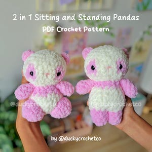 May include: Two handmade crochet panda bears in pink and white. The pandas have black eyes and pink accents on their ears, arms, and legs. The image includes text that reads "2 in 1 Sitting and Standing Pandas PDF Crochet Pattern".