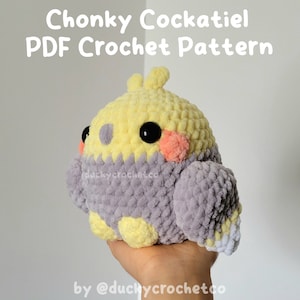 Op de afbeelding: Een gehaakt kaketoe pluche speelgoed met geel, grijs en wit garen. Het speelgoed heeft zwarte ogen en roze wangen. Het speelgoed wordt in de hand van een persoon gehouden. Chonky Cockatiel PDF Crochet Pattern by @duchycrochetco