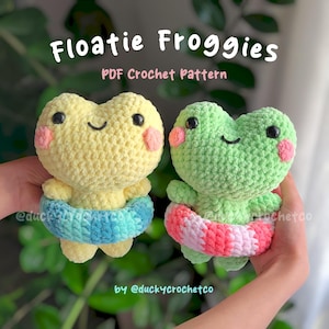 Puede incluir: Dos peluches de rana de crochet que llevan anillos inflables de colores. Las ranas son amarillas y verdes con mejillas rosadas y ojos negros. El texto "Floatie Froggies PDF Crochet Pattern by @duckycrochetco" está en la parte superior de la imagen.