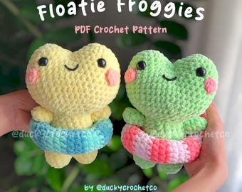 May include: Two crocheted frog plushies wearing colorful inflatable rings. The frogs are yellow and green with pink cheeks and black eyes. The text "Floatie Froggies PDF Crochet Pattern by @duckycrochetco" is at the top of the image.