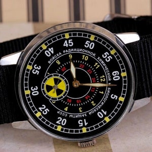 May include: A black wristwatch with a silver case and a black nylon strap. The watch face has a black background with white and yellow markings. The watch face also has a smaller circular dial with a yellow and black radiation symbol. The watch face has the text "ВОЙСКА РАДИАЦИОННОЙ, ХИМИЧЕСКОЙ И БИОЛОГИЧЕСКОЙ ЗАЩИТЫ СССР" around the outer edge.