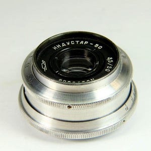 May include: A silver camera lens with the text "Индустар - 60 3,5/50" printed on the front.