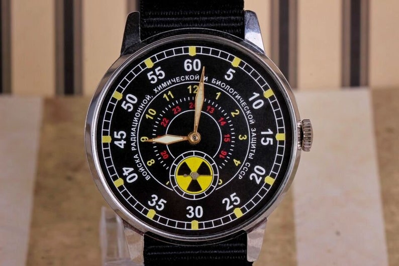 May include: A black wristwatch with a silver case and black band. The watch face has a black background with yellow and red markings. The watch face also has a yellow and black radiation symbol.