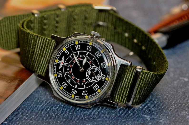 May include: A silver wristwatch with a black face and yellow markings. The watch has a green nylon strap.