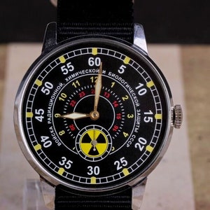 May include: A black wristwatch with a yellow and red radiation symbol on the face. The watch face has white numbers and text that reads "Войска Радиационной, Химической и Биологической Защиты СССР".