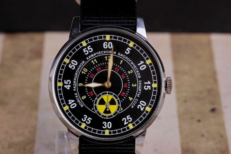 May include: A black wristwatch with a yellow and red radiation symbol on the face. The watch face has white numbers and text that reads "Войска Радиационной, Химической и Биологической Защиты СССР".