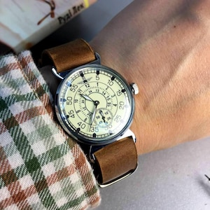 Puede incluir: Un reloj de pulsera plateado con una esfera blanca y una correa de cuero marr&oacute;n. La esfera del reloj tiene n&uacute;meros y manecillas negros, y un peque&ntilde;o dial de segundero en la parte inferior. El reloj est&aacute; en la mu&ntilde;eca de una persona.