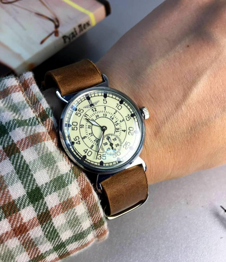 Puede incluir: Un reloj de pulsera plateado con una esfera blanca y una correa de cuero marr&oacute;n. La esfera del reloj tiene n&uacute;meros y manecillas negros, y un peque&ntilde;o dial de segundero en la parte inferior. El reloj est&aacute; en la mu&ntilde;eca de una persona.