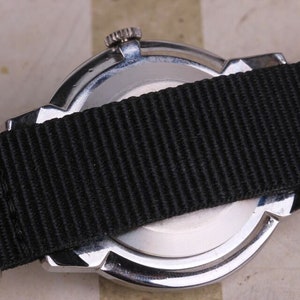 May include: A silver watch with a black nylon strap. The watch has a round face and a silver case. The strap is attached to the watch with two silver lugs.