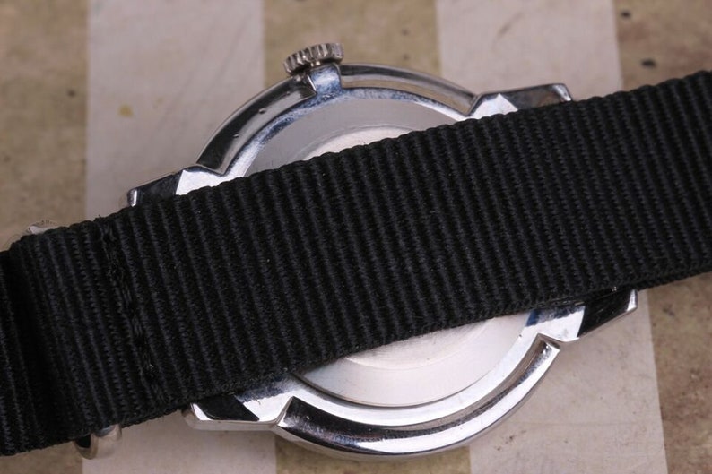 May include: A silver watch with a black nylon strap. The watch has a round face and a silver case. The strap is attached to the watch with two silver lugs.