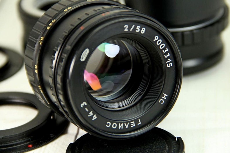 Puede incluir: Lente de c&aacute;mara negra con el texto "2/58" y "9003315" en blanco. La lente tiene un anillo de enfoque estriado y un elemento de vidrio reflectante. Otras partes de la c&aacute;mara son visibles en el fondo.