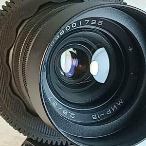Op de afbeelding: Close-up van een zwarte cameralens met de tekst "2.8/37" en "MИP-1B". De lens heeft een reflecterend oppervlak en is omgeven door een zwarte, getextureerde ring. De lens is ontworpen voor fotografie.
