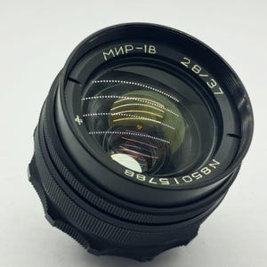 May include: A black MIR-1B 2.8/37 camera lens with white lettering. The lens has a ridged focus ring and a reflective glass element. The serial number N85015788 is visible on the lens.