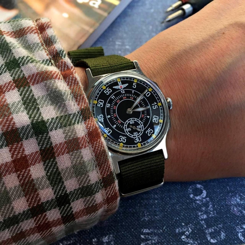 May include: A black and white wristwatch with a green nylon strap. The watch face has a black background with white numbers and a red second hand. The watch face also has a small white dial with black numbers.