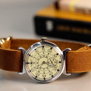 Puede incluir: Un reloj de pulsera plateado con una esfera blanca y agujas negras. El reloj tiene una correa de cuero marr&oacute;n y un dial de segundero. La esfera del reloj tiene n&uacute;meros del 5 al 60.