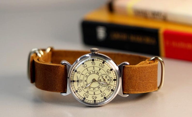 Puede incluir: Un reloj de pulsera plateado con una esfera blanca y agujas negras. El reloj tiene una correa de cuero marr&oacute;n y un dial de segundero. La esfera del reloj tiene n&uacute;meros del 5 al 60.