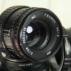 Puede incluir: Primer plano de una lente negra Helios 44-3 con el texto "ГЕЛИОС" y "2/58". La lente tiene marcas de medici&oacute;n y el n&uacute;mero "9003315". Otros componentes de la lente tambi&eacute;n son visibles.