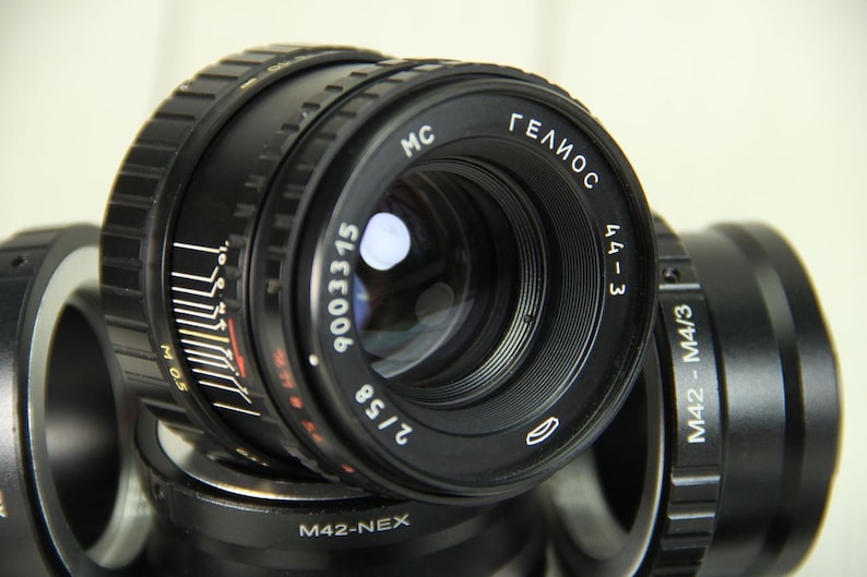 Puede incluir: Primer plano de una lente negra Helios 44-3 con el texto "ГЕЛИОС" y "2/58". La lente tiene marcas de medici&oacute;n y el n&uacute;mero "9003315". Otros componentes de la lente tambi&eacute;n son visibles.