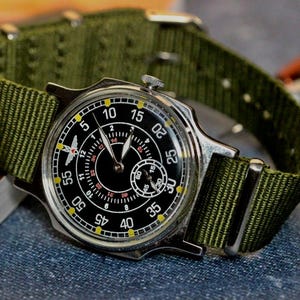 May include: A silver wristwatch with a black face and yellow markings. The watch has a green nylon strap.