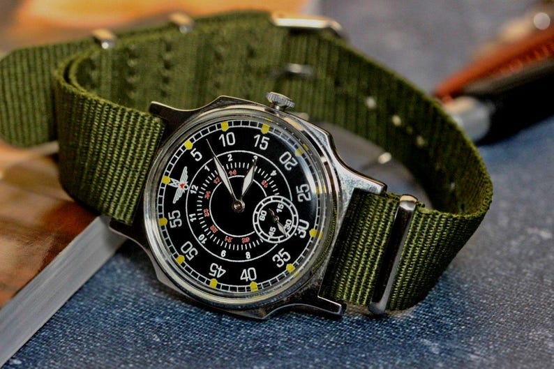 May include: A silver wristwatch with a black face and yellow markings. The watch has a green nylon strap.