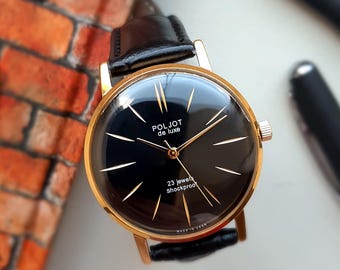 Könnte beinhalten: Eine Vintage Poljot de luxe Armbanduhr mit schwarzem Zifferblatt, goldenen Zeigern und einem goldfarbenen Gehäuse. Die Uhr hat ein schwarzes Lederarmband und der Text "23 jewels shockproof" ist sichtbar. Die Uhr ist mit "Made in USSR" gekennzeichnet.