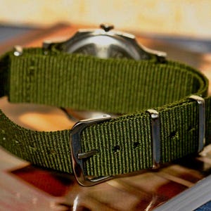 May include: A green nylon watch strap with silver buckle and keeper.