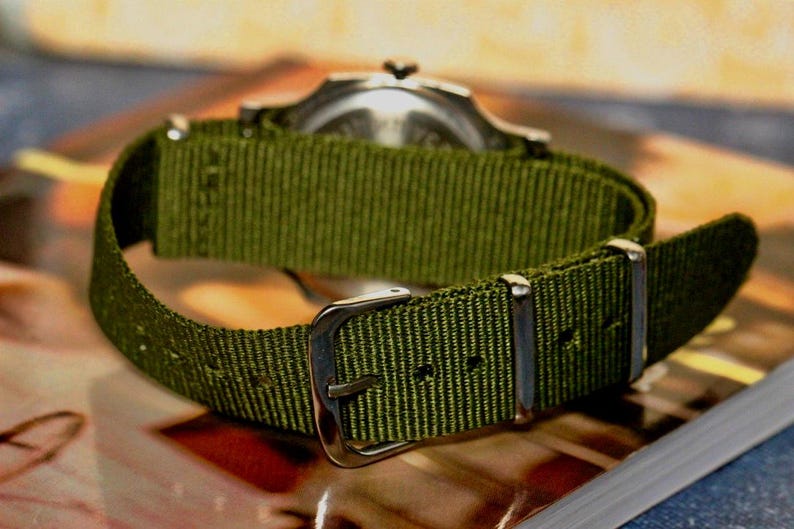 May include: A green nylon watch strap with silver buckle and keeper.