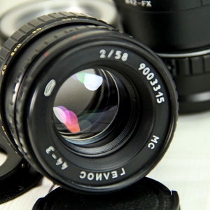 Puede incluir: Un objetivo de c&aacute;mara negro con el texto "2/58" y "9003315" impreso en la parte delantera. El objetivo tiene una superficie reflectante y est&aacute; rodeado de otros accesorios de c&aacute;mara. Es un producto de fotograf&iacute;a.