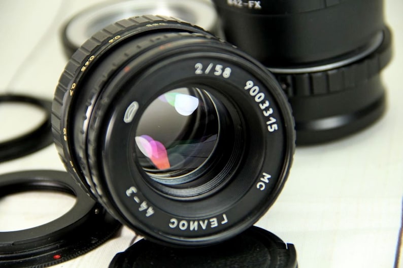 Puede incluir: Un objetivo de c&aacute;mara negro con el texto "2/58" y "9003315" impreso en la parte delantera. El objetivo tiene una superficie reflectante y est&aacute; rodeado de otros accesorios de c&aacute;mara. Es un producto de fotograf&iacute;a.