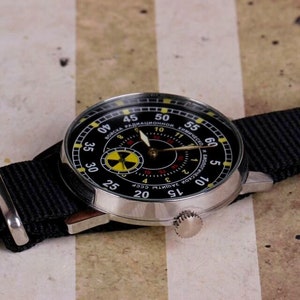 May include: A black wristwatch with a silver case and a black nylon strap. The watch face has a black background with yellow and red markings. The text on the watch face reads "СОЮЗ РАДИАЦИОННОЙ ЗАЩИТЫ СССР".