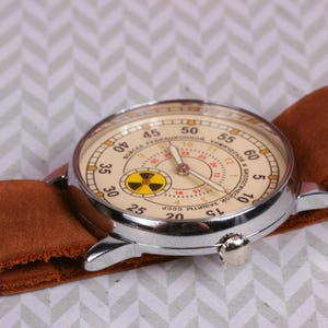 May include: A vintage wristwatch with a brown leather band and a white face with black markings. The watch face has a yellow and black radiation symbol in the center and the text "ЧАСОВЫЙ ЗАВОД ИМ. П.А.  ЧАЙКОВСКОГО СССР" around the edge.
