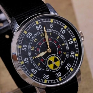 May include: A black wristwatch with a silver case and a black nylon strap. The watch face has a black background with yellow and red markings. The watch face also has a yellow and black radiation symbol in the center. The watch face has the text "РАДИАЦИОННОЙ, ХИМИЧЕСКОЙ" and "ВОИСКА" in Cyrillic script. The watch face also has the text "БИОЛОГИЧЕСКОЙ ЗАЩИТЫ СССР" in Cyrillic script.
