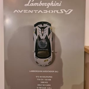 Puede incluir: Un coche modelo Lamborghini Aventador SVJ blanco con detalles amarillos. El coche tiene un interior negro y un alerón negro. El coche está sobre un fondo blanco con texto que dice "Lamborghini Aventador SVJ", "V12 48 Soupapes", "770 CV/720 NM", "1600 KG", "Only 63 Cars", "0-100 km/h 2,8 s", y "V Max > 350 km/h".